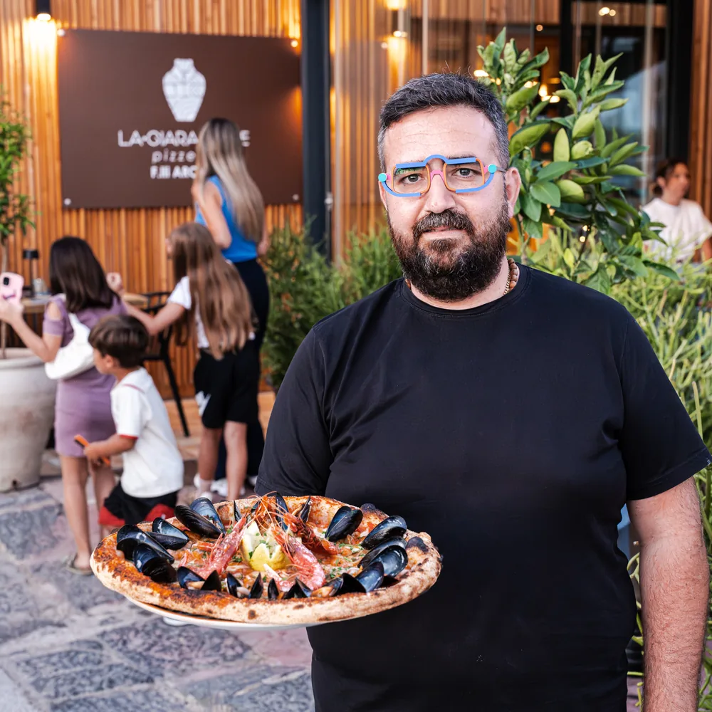 Il pizzaiolo con una pizza ai frutti di mare appena sfornata